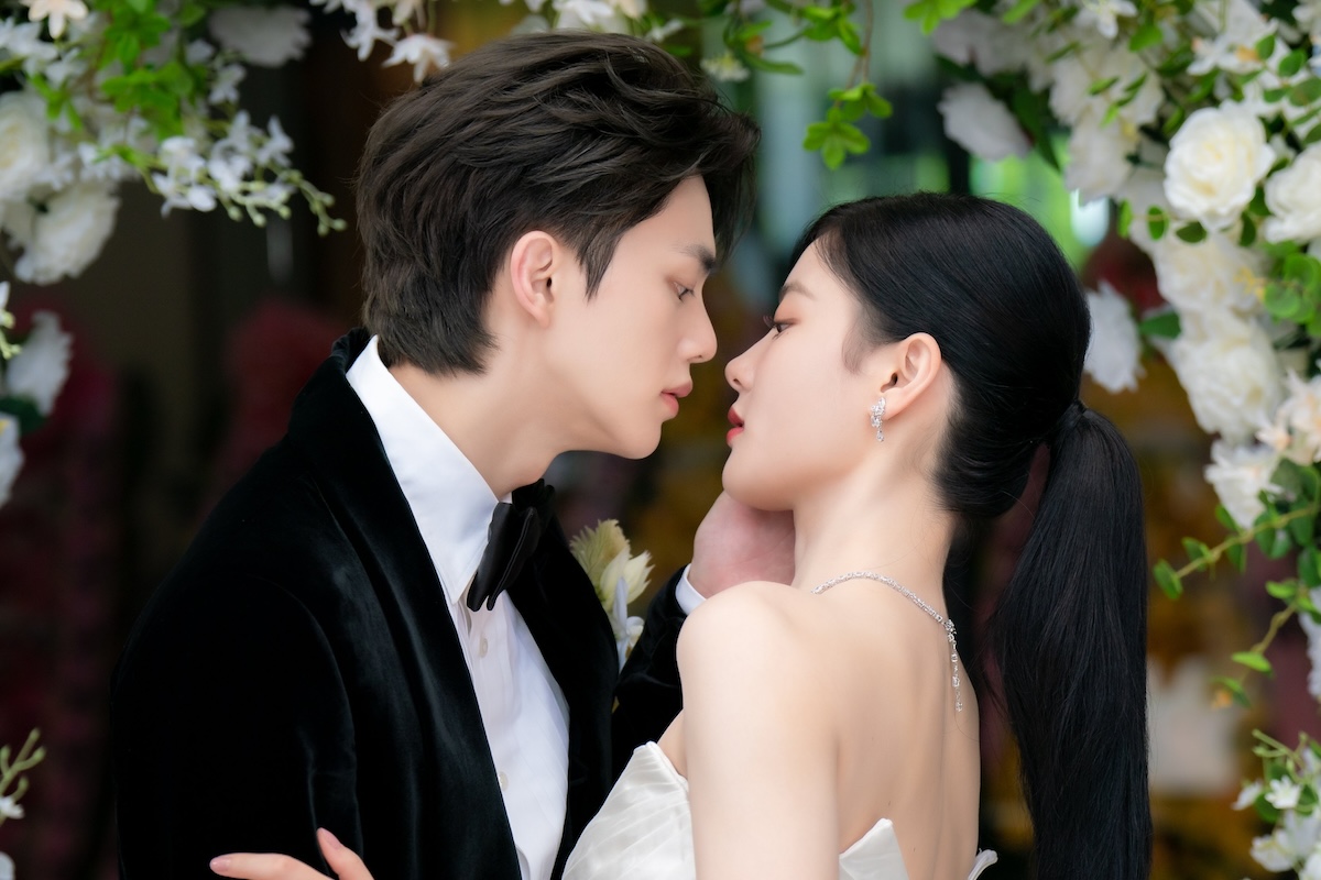 A couple in wedding outfits leaning in for a kiss beneath a flowering tree